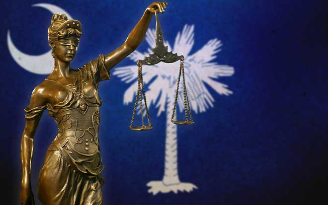 A statue holds up a weight scale behind the South Carolina flag