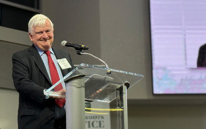 Stan Jones in black suit with red tie receiving award at podium