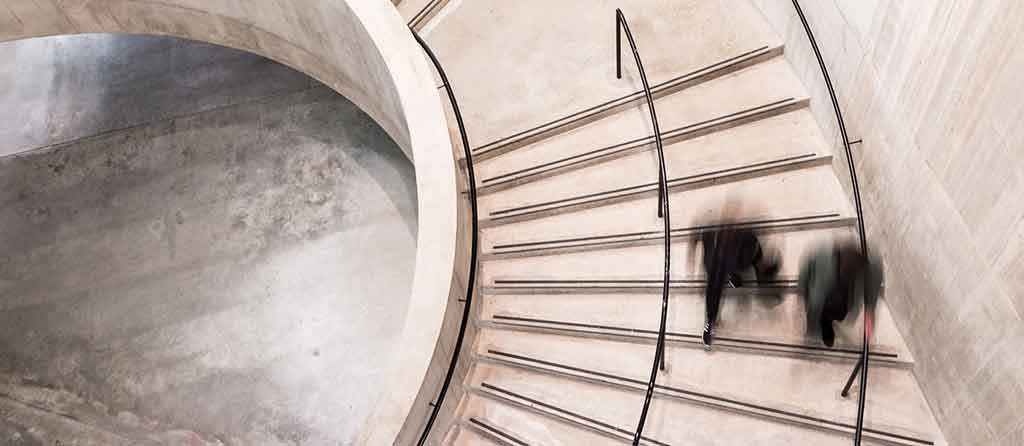 Image of two individuals quickly walking down a spiral staircase